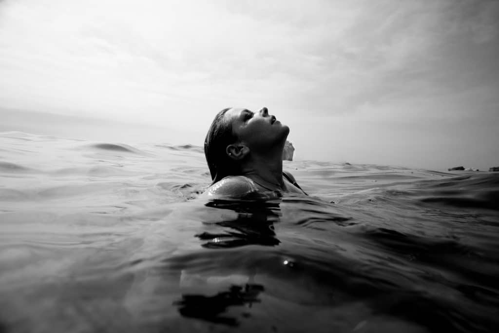 Mulher nadando no mar com a cabeça para fora como se estivesse pegando fôlego. 