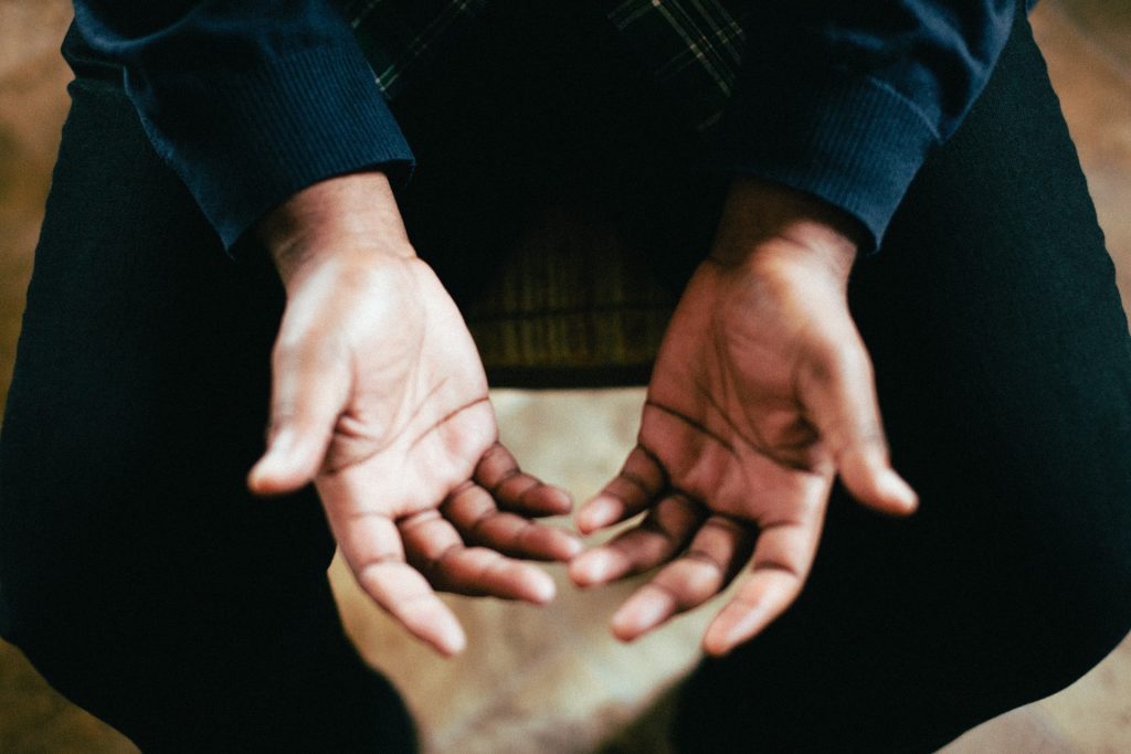 Pessoa sentada com as palmas das mãos voltadas para cima, em sinal de oração.