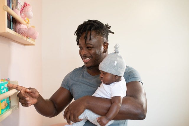 Pai segurando filho no colo mostrando brinquedo na prateleira sorrindo