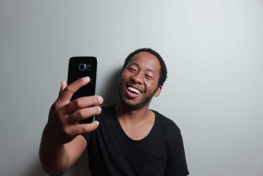 Homem tirando selfie sorrindo em parede branca