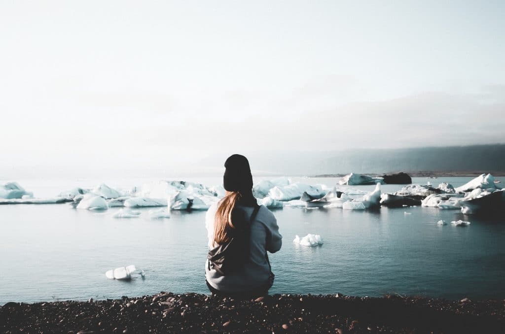 Mulher sentada de costas em frente ao oceano com icebergs.