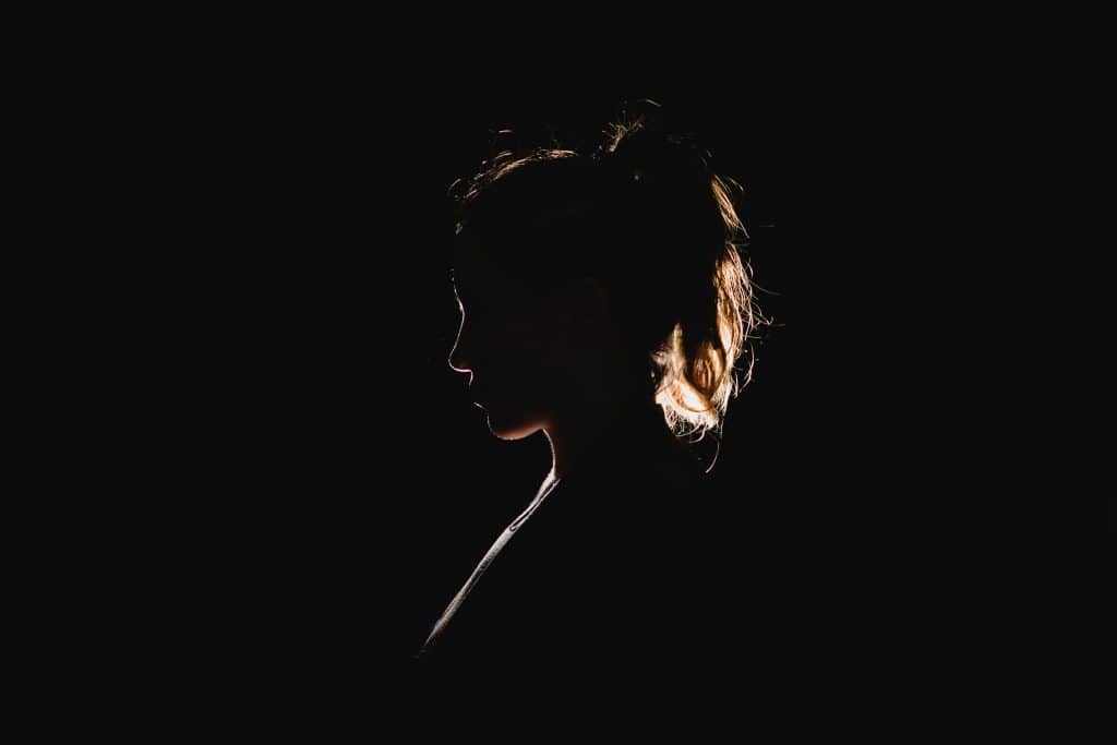 Silhueta de mulher com cabelos presos de perfil em fundo escuro