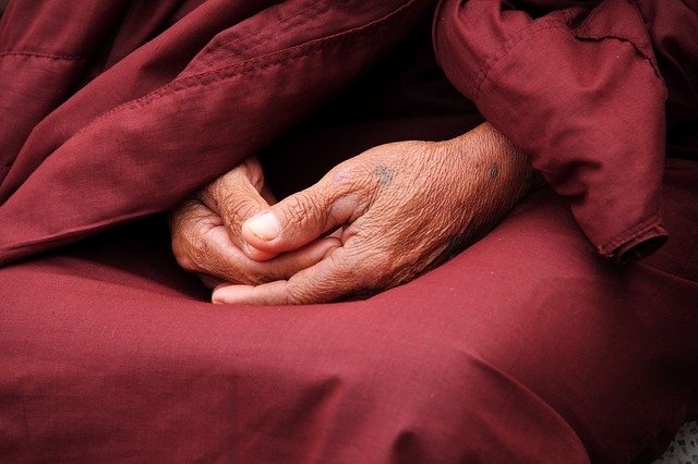 Mãos de monge unidas em seu colo