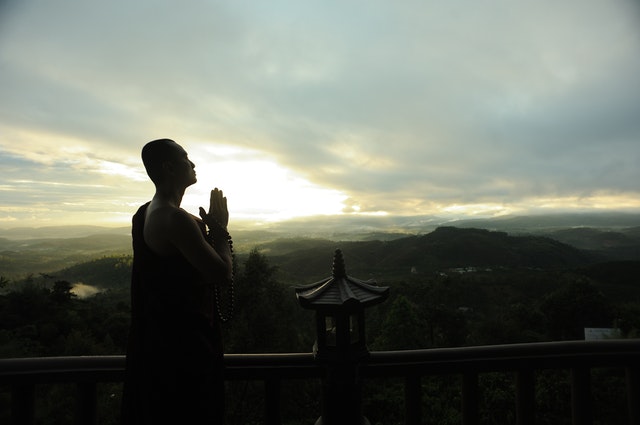 Monge em templo olhando pôr-do-sol e céu nublado