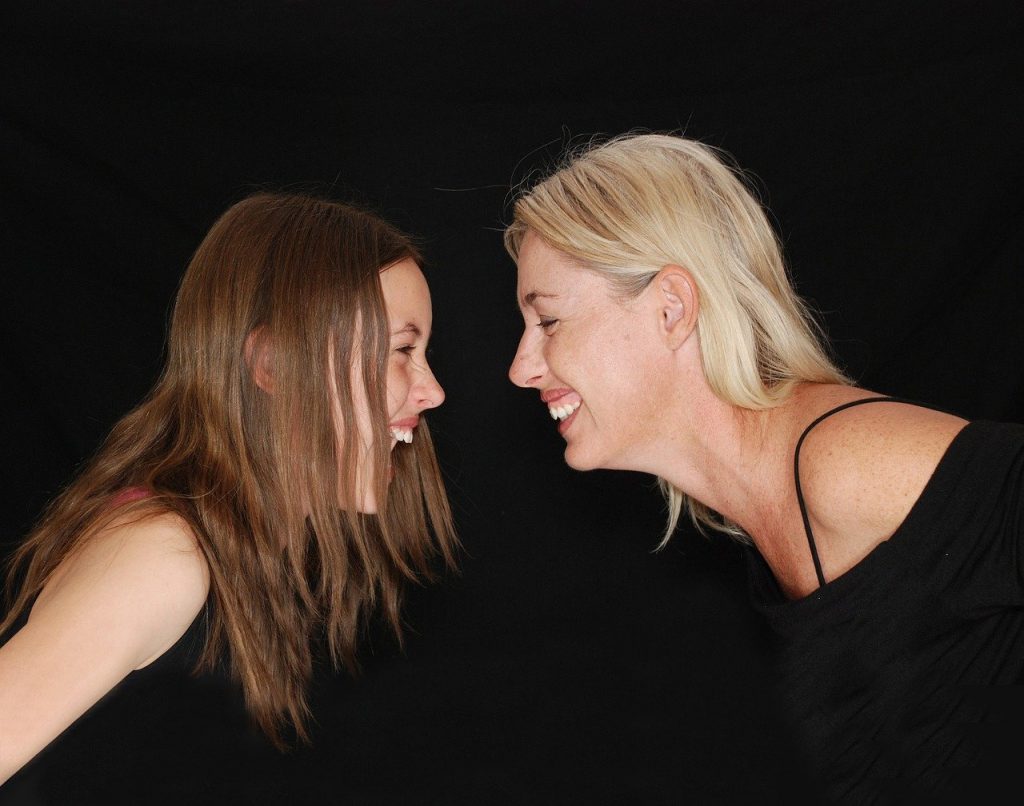 Imagem de mãe e filha uma de frente para a outra. Elas estão felizes e sorrindo.