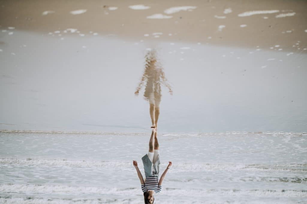 Mulher caminhando à beira da praia, com sua imagem refletida na água do mar.