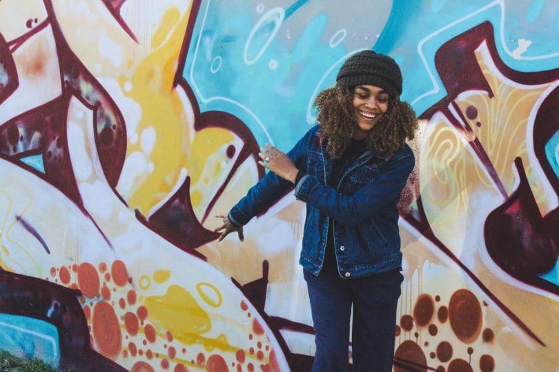 Mulher sorrindo com os olhos fechados de frente para um muro colorido