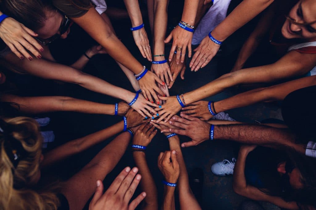 Grupo de pessoas em círculo com as mãos unidas ao meio.