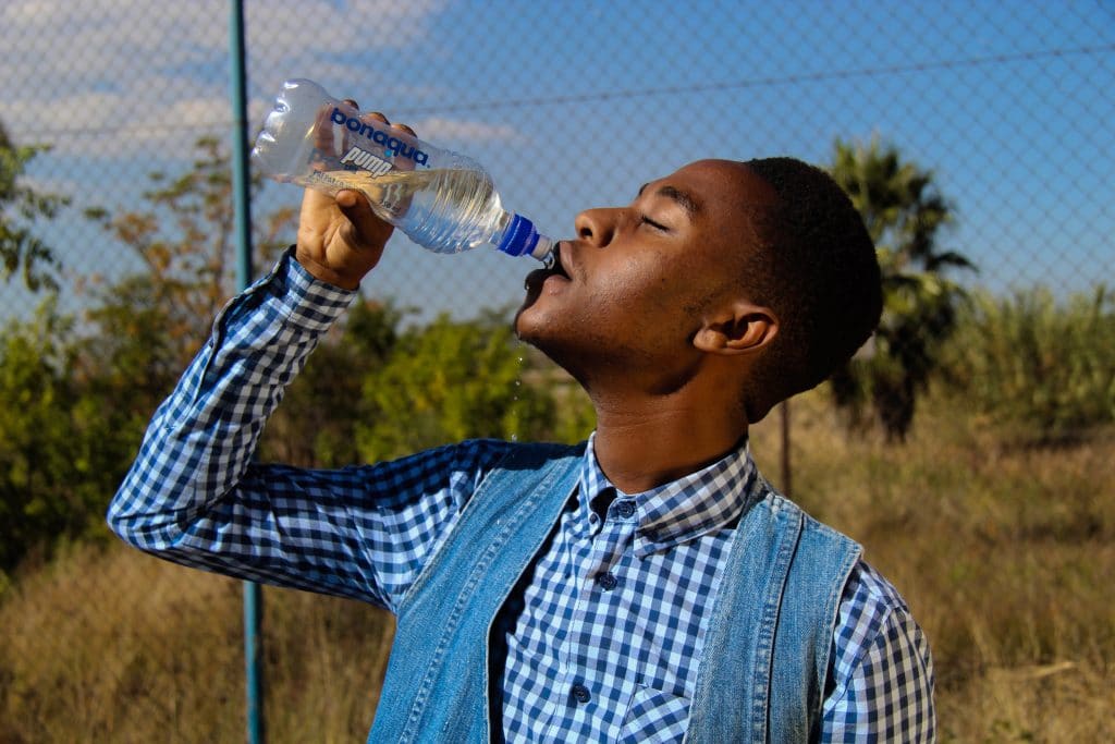 Homem de perfil bebendo água de uma garrafa plástica.