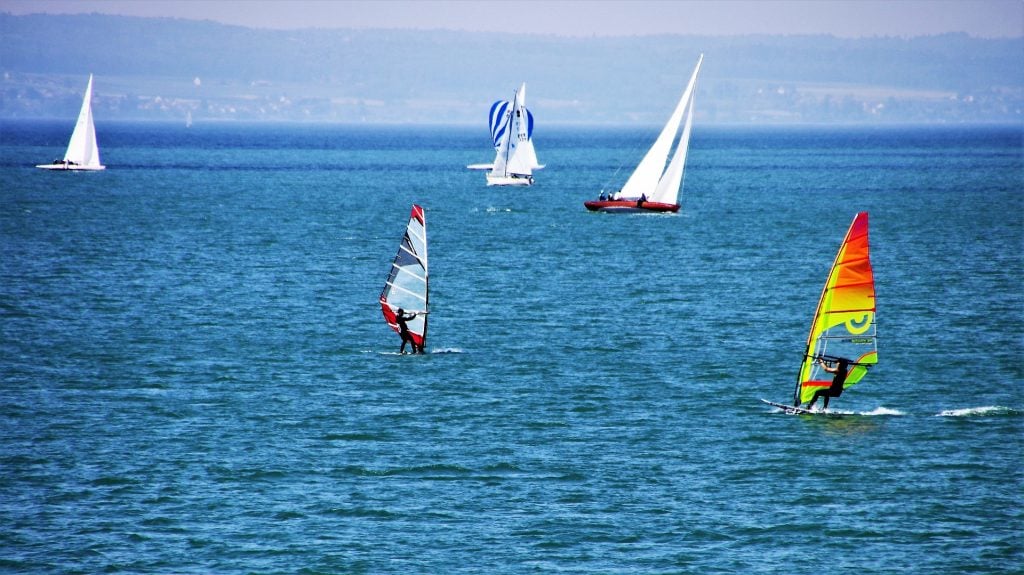 Homens participando de uma competição de veleiro em um lindo lago azul.
