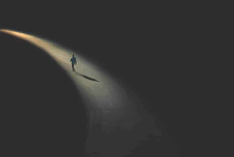 Homem andando sozinho em um trecho iluminado de uma rua durante a noite