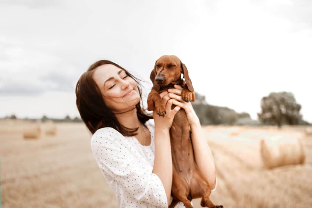 Mulher segurando cachorro no colo de olhos fechados em campo aberto