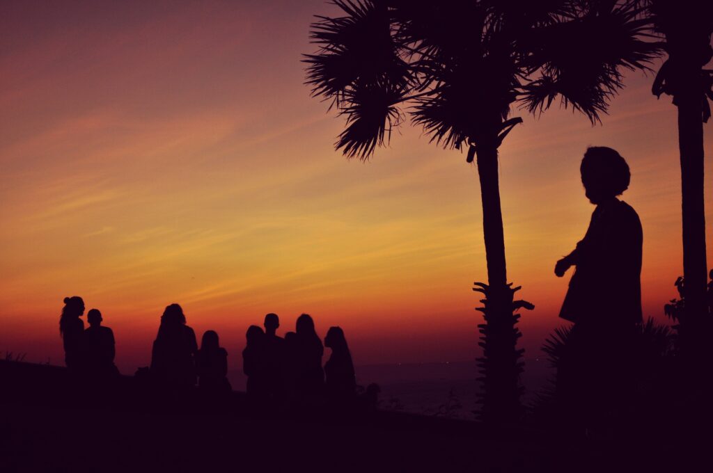 Imagem de um grupo de pessoas e um líder do estilo reggae em um campo alto assistindo o pôr do sol.