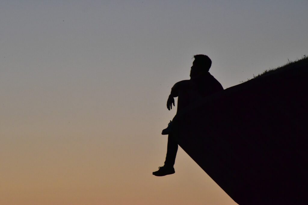 Silhueta de um homem pensando. Ele está sentado no pico de uma montanha.