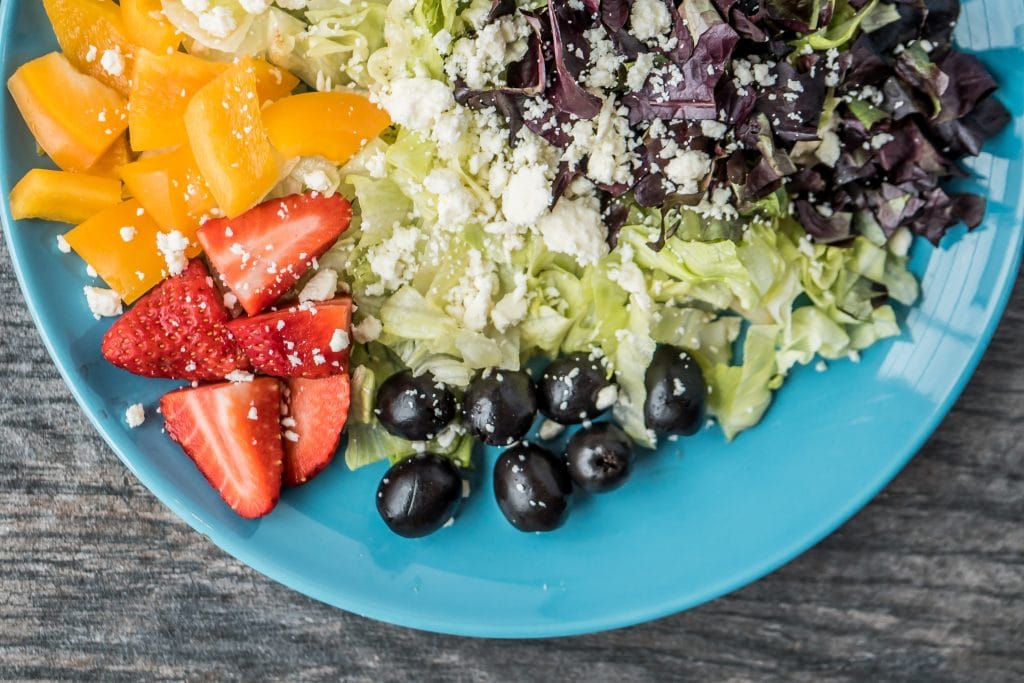 Prato de salada com folhas, azeitonas e frutas.