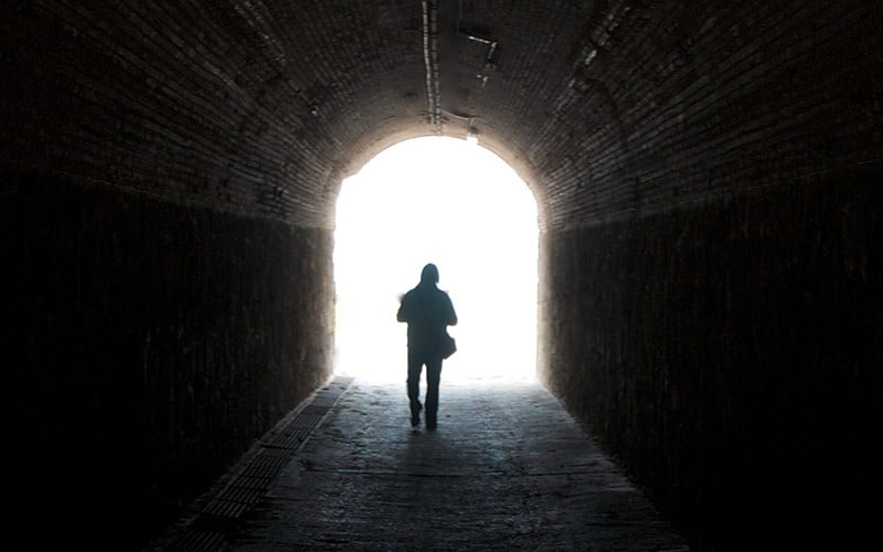 Silhueta de um homem atravessando um túnel escuro, em direção à luz em seu fim.