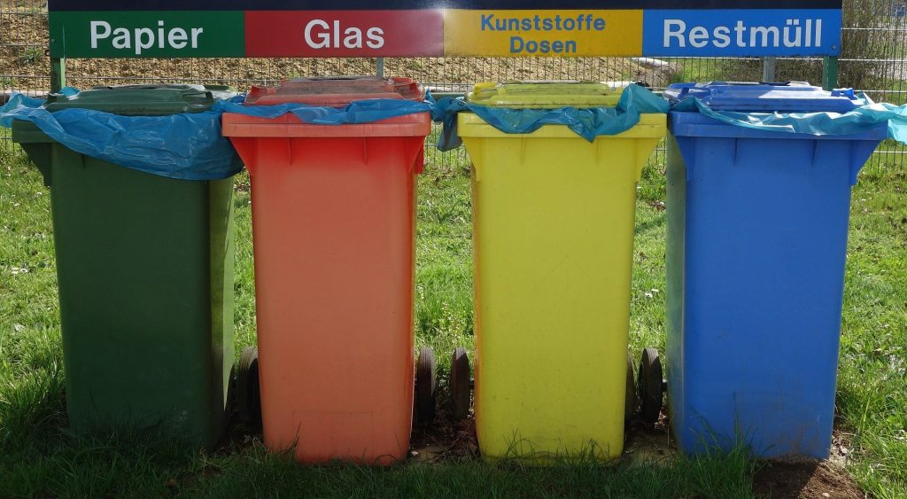 Imagem de latões para a separação de resíduos nas cores: verde, laranja, amarelo e azul.
