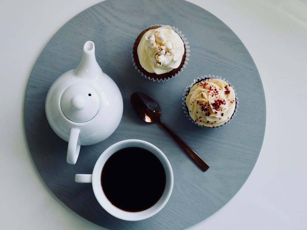 Bandeja com um bule, uma xícara de café, uma colher e dois cupcakes.