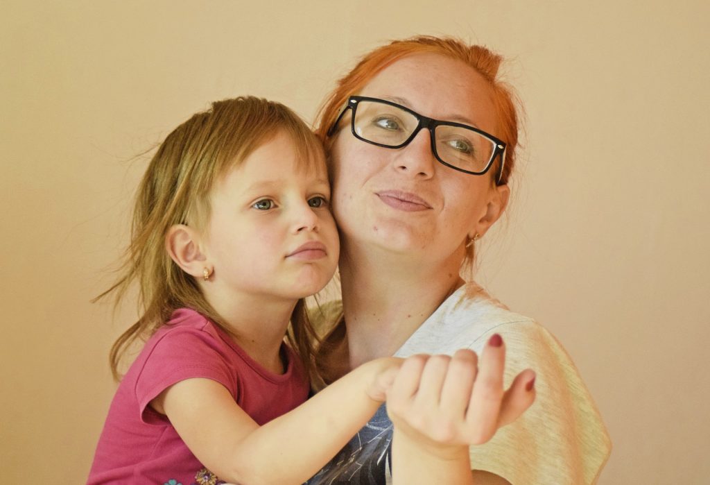 Imagem de mãe e filha. A mãe está com a criança no colo e segura a sua mão.
