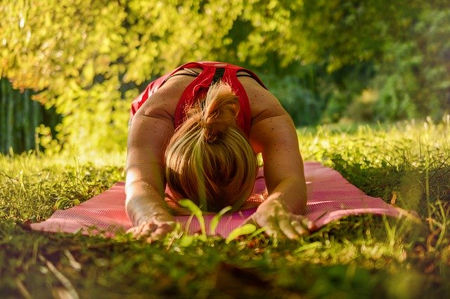 Mulher fazendo Yoga em tapete em grama com área verde