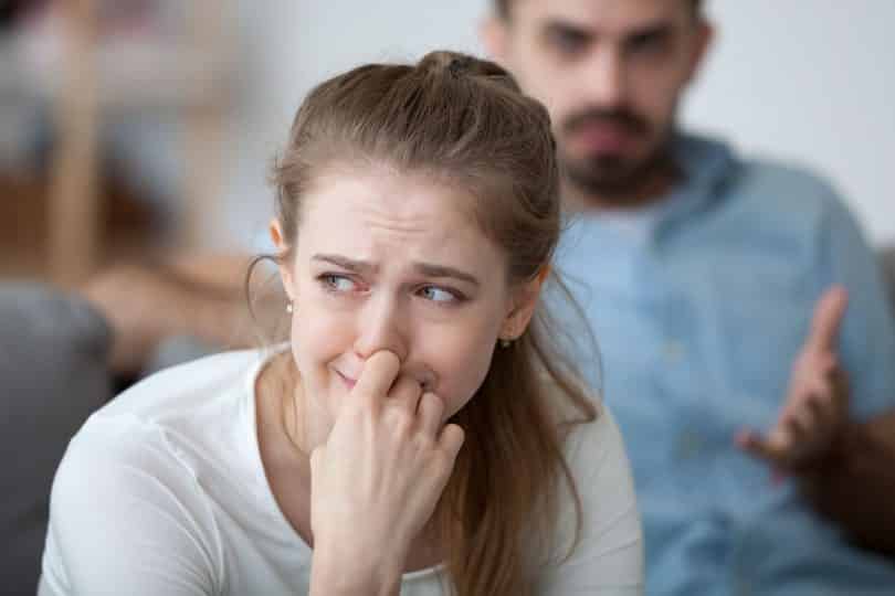 Mulher triste chorando com a mão sobre o rosto enquanto um homem a encara com expressão nervosa.