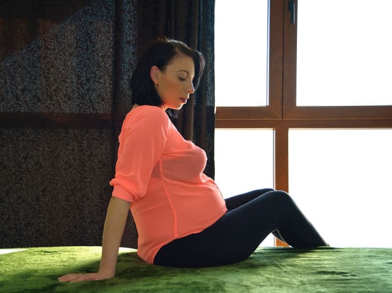 Mulher madura grávida, sentada, e apoiada com os braços para trás.