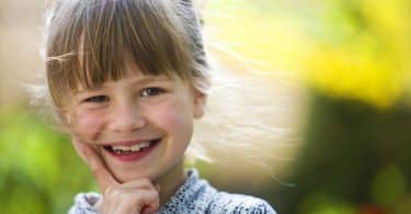 Menina pequena, com cabelo preso e franja na testa, sorrindo para a câmera.