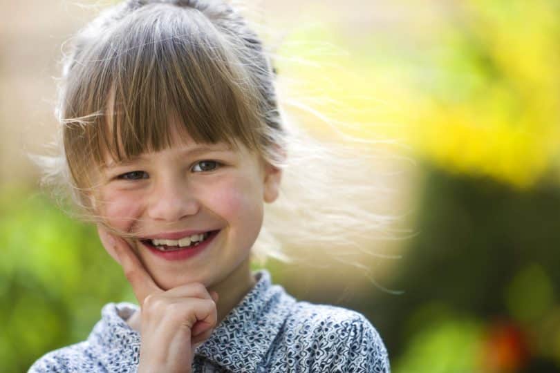 Menina pequena, com cabelo preso e franja na testa, sorrindo para a câmera.