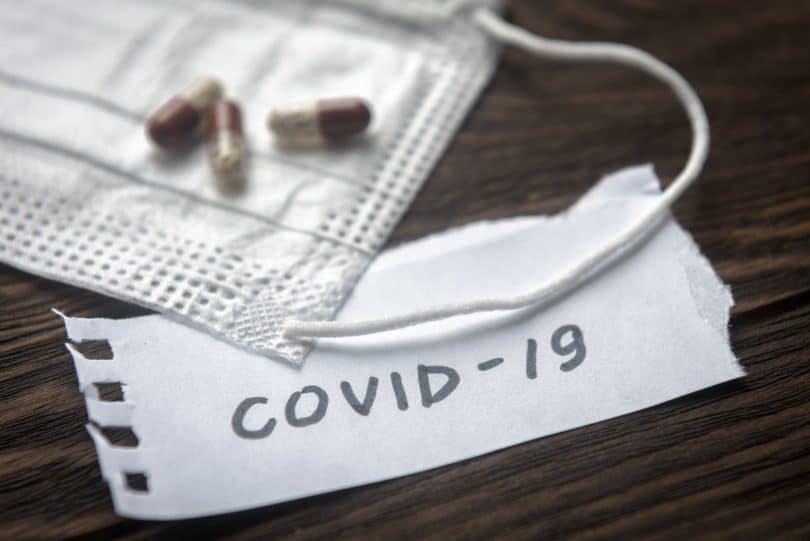 Máscara de proteção com alguns comprimidos e um bilhete escrito COVID-19