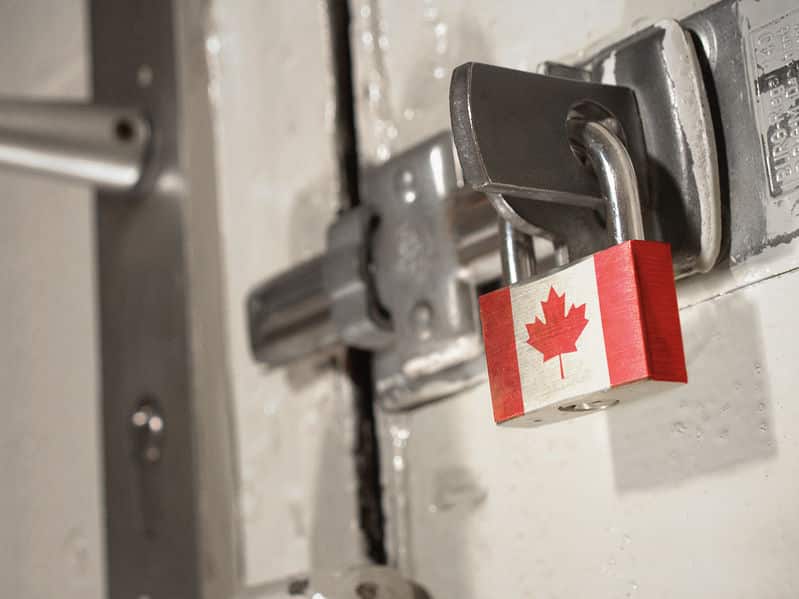 Porta trancada com fechadura de ferro, presa com um cadeado com a bandeira do Canadá.