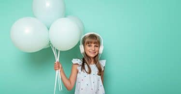 Menina pequena com fones de ouvido e segurando balões.