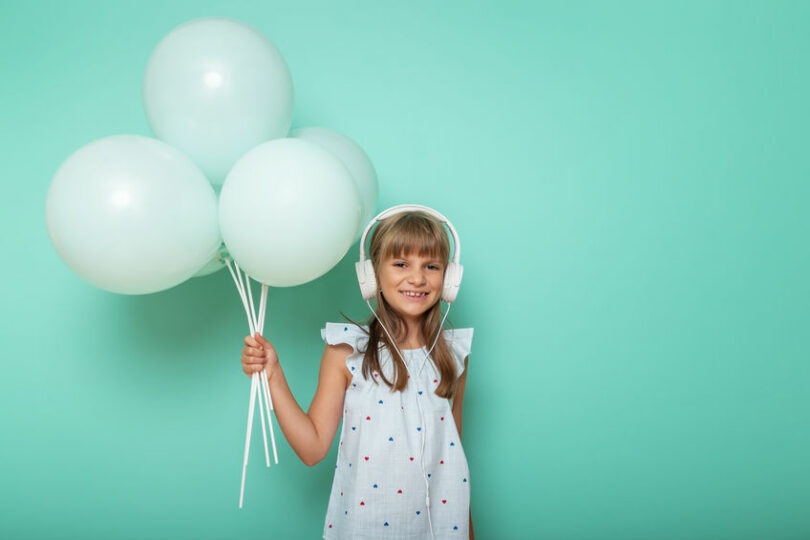 Menina pequena com fones de ouvido e segurando balões.