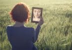 Mulher se olhando no espelho em um campo, durante o dia.