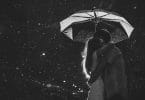 Casal abraçado segurando guarda-chuva com céu estrelado ao fundo