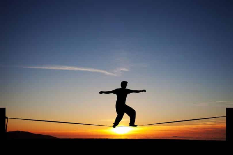 Silhueta de homem andando em slack line com sol ao fundo