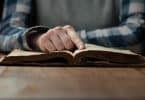 Mão apoiada em bíblia aberta sobre a mesa