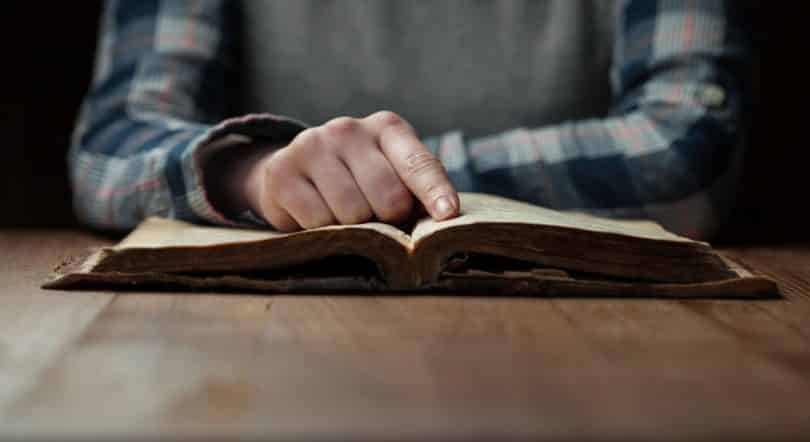 Mão apoiada em bíblia aberta sobre a mesa