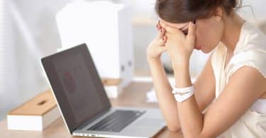 Mulher sentada em uma mesa de escritório, com a cabeça apoiada sobre as mãos, em sinal de estresse.