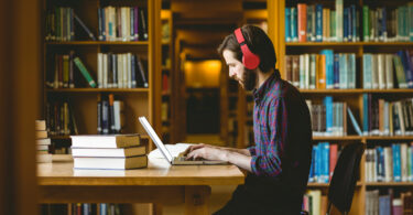 Homem sentado em uma biblioteca, estudando.