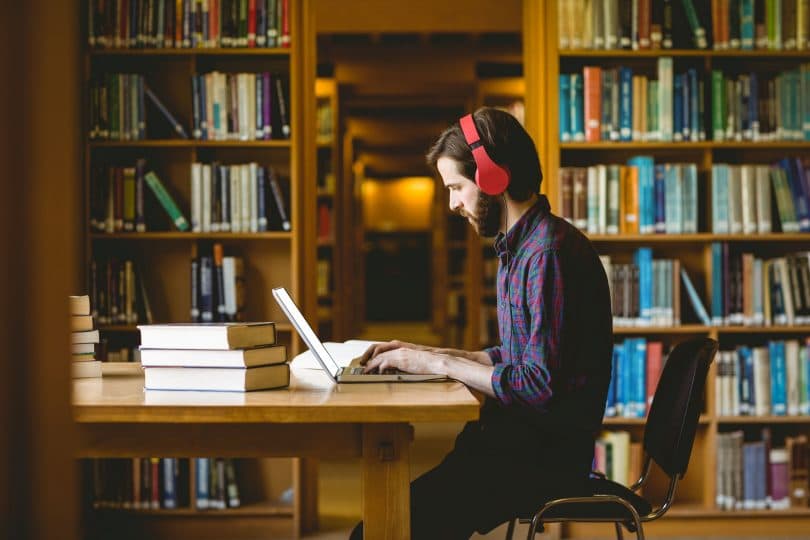 Homem sentado em uma biblioteca, estudando.