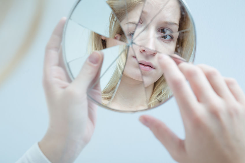 Mulher segurando espelho quebrado, olhando seu reflexo.