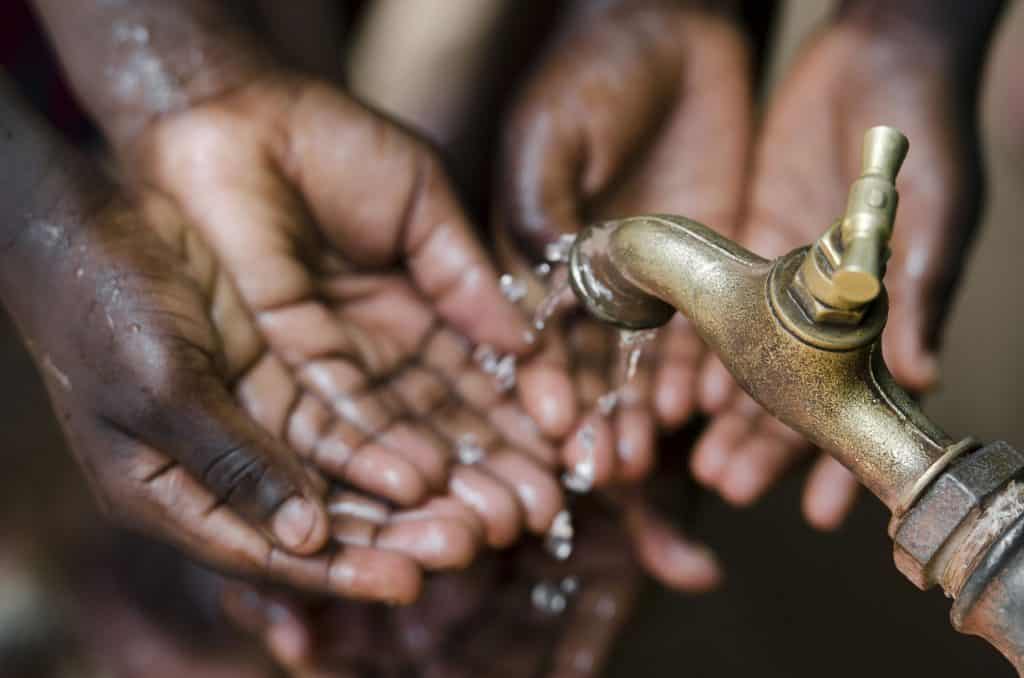 Pessoas lavando as mãos em uma torneira com pouca água