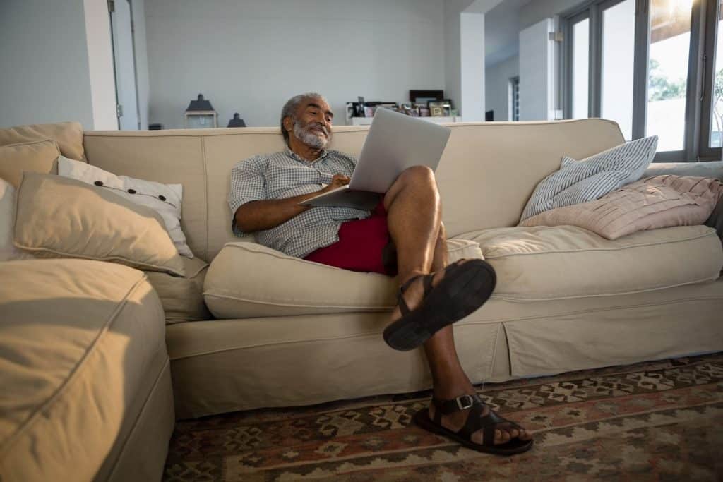 Senhor sentado em um sofá com um notebook no colo.