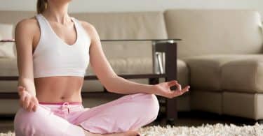 Mulher sentada no chão da sala de estar, meditando.