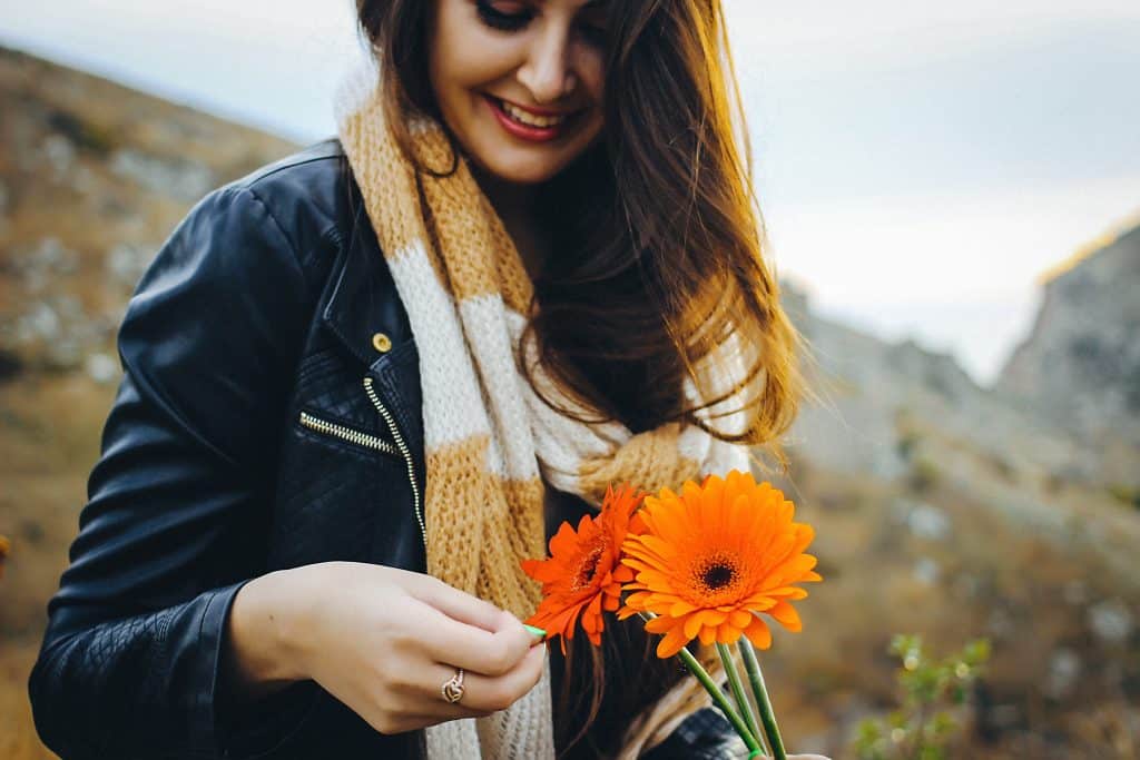 Mulher sorrindo segurando flor em meio a montanhas