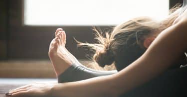 Mulher praticando Yoga com a cabeça sobre as pernas esticadas no chão.