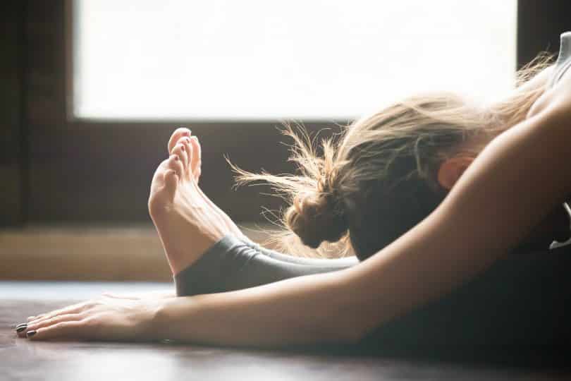 Mulher praticando Yoga com a cabeça sobre as pernas esticadas no chão.