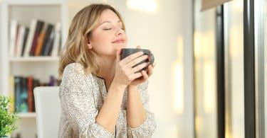 Mulher com os olhos fechados segurando caneca