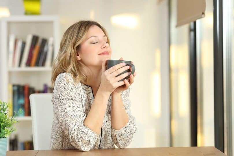 Mulher com os olhos fechados segurando caneca