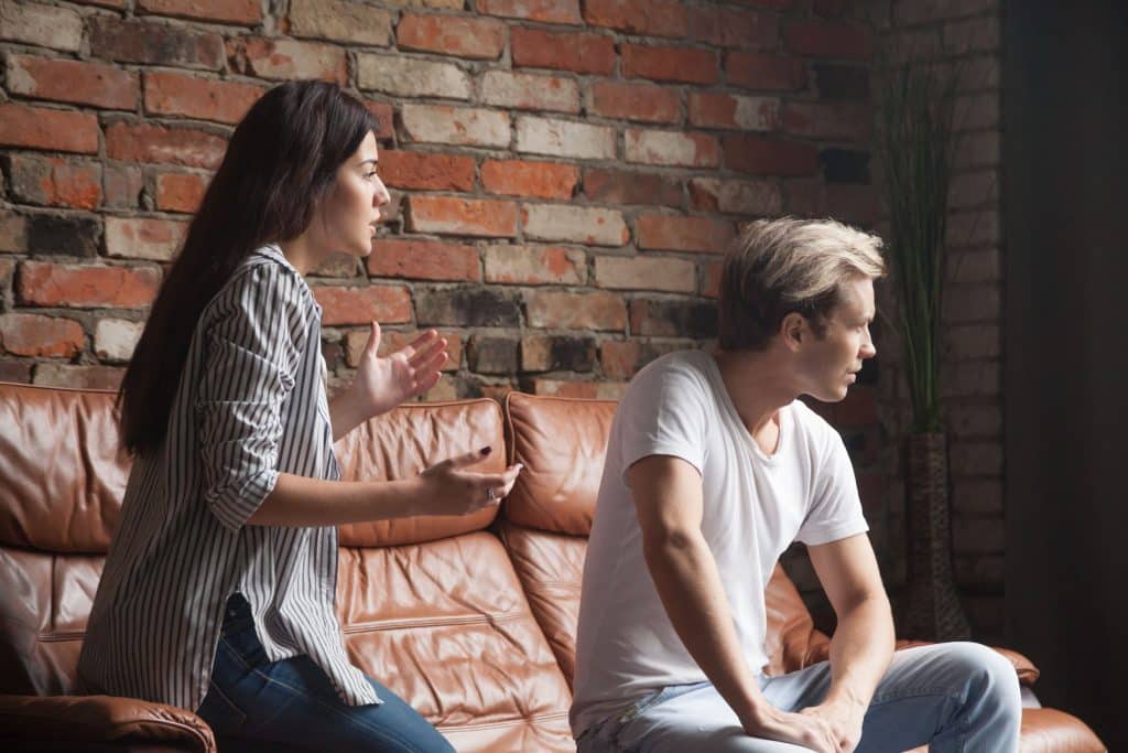 Mulher tenta discutir com um homem sentado no sofá, que a ignora.